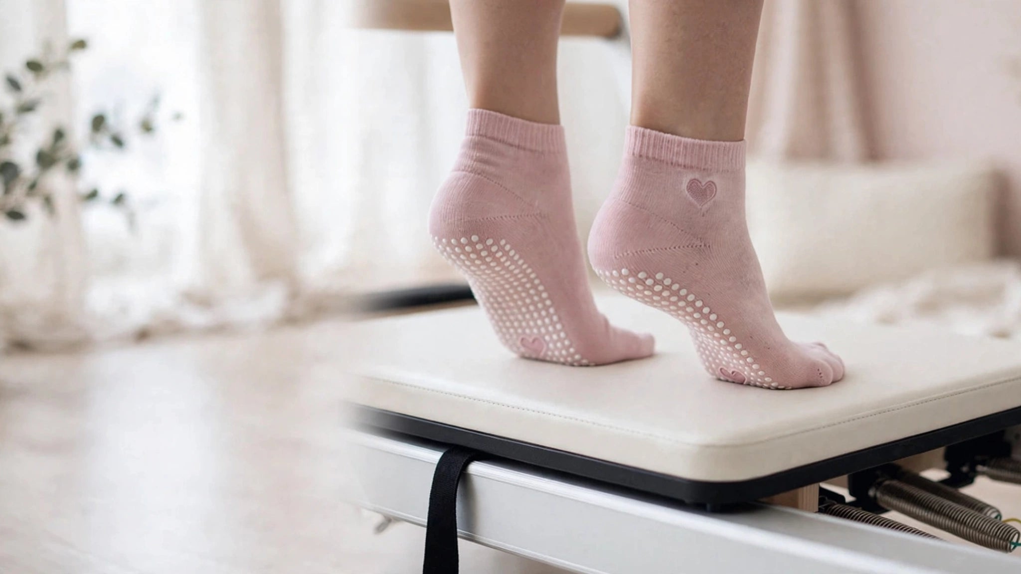 Feet in pink NOEILI grip socks with heart detail on a Pilates reformer